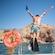 A man in flippers holding snorkeling gear jumps from a boat into the water